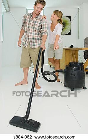 Stock Image - Woman pointing as man vacuums. Fotosearch
