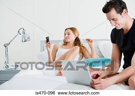 Couple on bed with laptop and handheld computer View Large Photo Image Stock Photograph - Couple on bed with laptop and handheld computer. Fotosearch