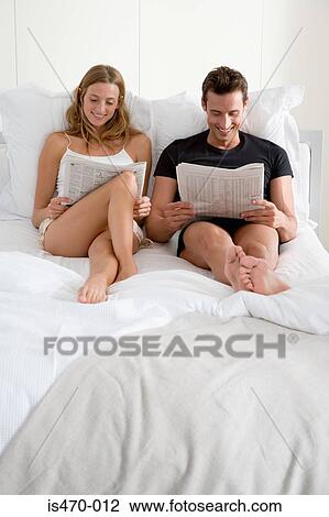 Stock Image - Couple reading newspapers on bed. Fotosearch