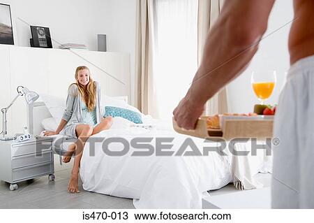 Stock Image - Man bringing breakfast in bed to woman. Fotosearch