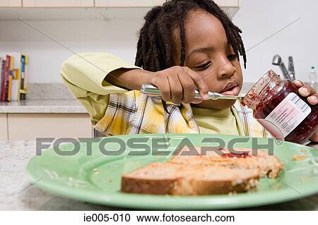Stock Image - Boy scooping jam out of jar. Fotosearch