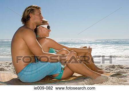 Stock Image - Couple sat on a beach. Fotosearch
