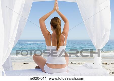 Stock Image - Woman practising yoga on a beach. Fotosearch