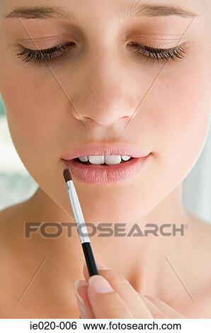 Stock Photograph - Young woman applying lipstick. Fotosearch