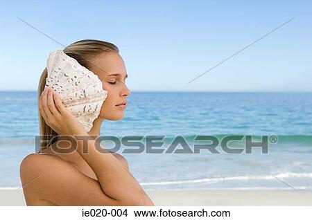 Picture - Young woman listening to shell. Fotosearch