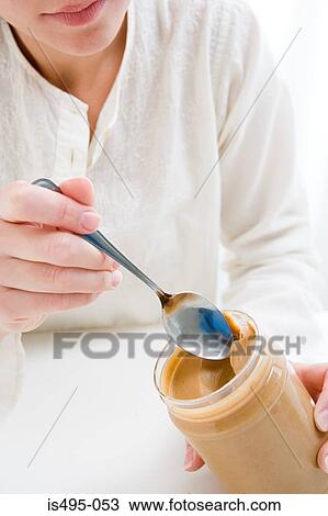 Stock Image - Woman scooping peanut butter from jar. Fotosearch