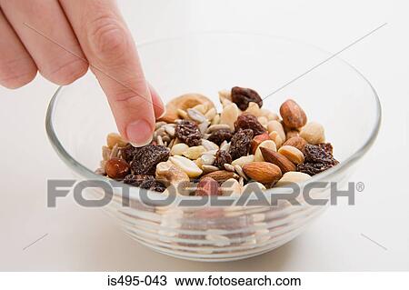 Stock Image - Young woman picking at a bowl of nuts. Fotosearch