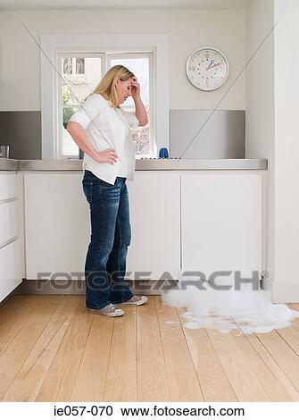 Stock Image - Woman looking at leaking dishwasher. Fotosearch
