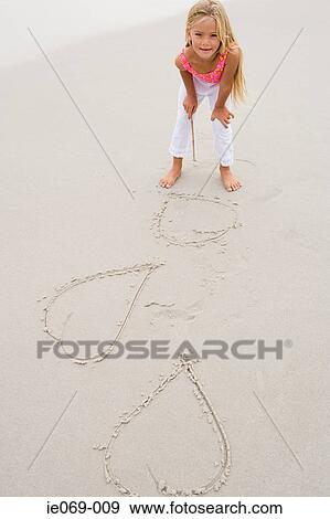 Stock Photo - Girl drawing hearts on the sand. Fotosearch