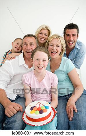 Girl holding a birthday cake surrounded by family View Large Photo Image Stock Photo - Girl holding a birthday cake surrounded by family. Fotosearch