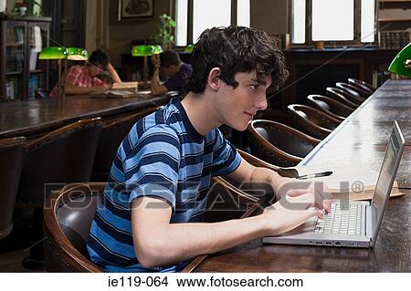 Picture - Boy using a laptop computer in library. Fotosearch