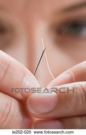 A woman threading cotton through a needle View Large Photo Image Stock Photography - A woman threading cotton through a needle. Fotosearch