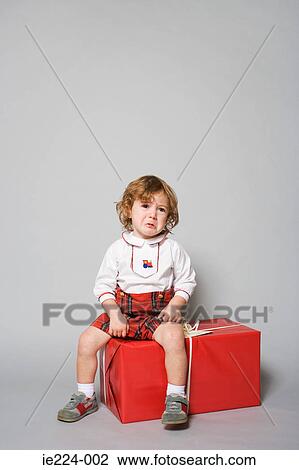 Stock Image - Sad boy sitting on a present. Fotosearch