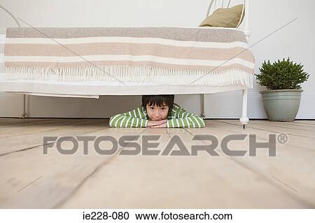 Stock Image - Boy hiding under a bed. Fotosearch