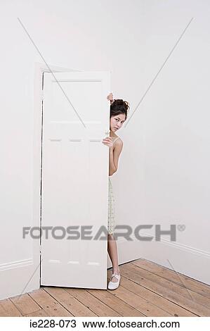Stock Image - Young woman hiding behind a door. Fotosearch