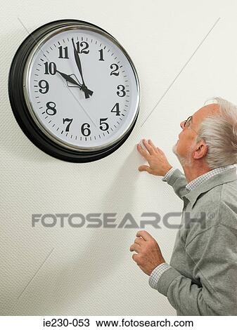 Stock Image - Senior man looking at a large clock. Fotosearch