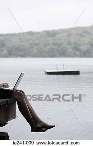 A woman with a laptop sat on a jetty View Large Photo Image Stock Photo - A woman with a laptop sat on a jetty. Fotosearch