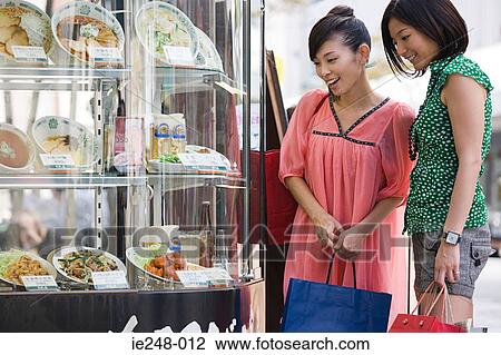 Stock Image - Friends looking in a restaurant window. Fotosearch