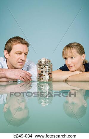 Picture - Couple looking at jar of coins. Fotosearch