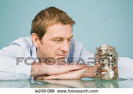 Man looking at jar of coins View Large Photo Image Stock Photo - Man looking at jar of coins. Fotosearch