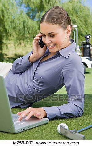 A businesswoman typing on a laptop and using a cell phone View Large Photo Image Stock Image - A businesswoman typing on a laptop and using a cell phone. Fotosearch