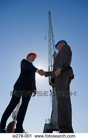 Stock Image - Men shaking hands by crane. Fotosearch