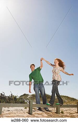 Stock Image - A young man helping a woman balancing on a fence. Fotosearch
