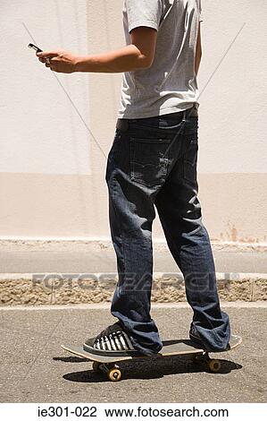 A teenage boy skateboarding and using a cell phone View Large Photo Image Stock Image - A teenage boy skateboarding and using a cell phone. Fotosearch