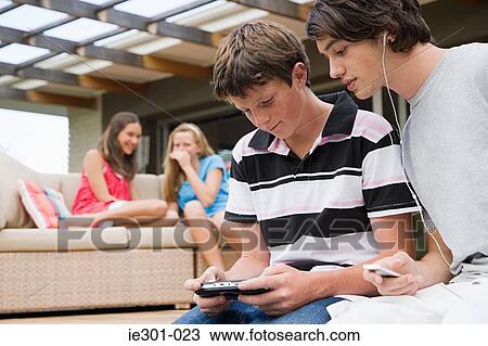 Teenage boys listening to music and playing a video game View Large Photo Image Stock Image - Teenage boys listening to music and playing a video game. Fotosearch