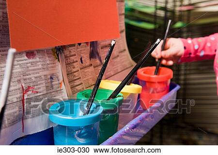 Stock Image - A girl putting a paintbrush in a paint pot. Fotosearch