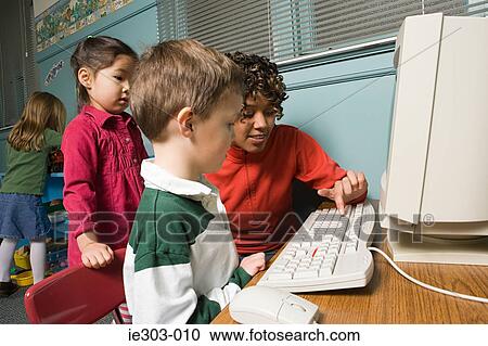 Stock Image - A teacher showing her pupils how to use a computer. Fotosearch