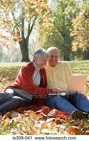 Senior couple using a laptop in a park View Large Photo Image Stock Image - Senior couple using a laptop in a park. Fotosearch