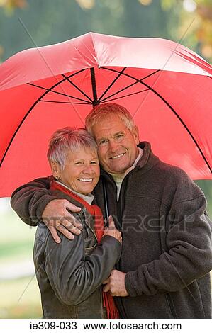 Stock Image - Senior couple using a red umbrella. Fotosearch