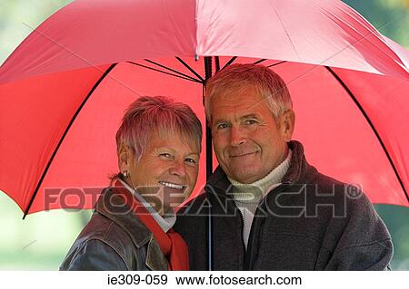 Senior couple using a red umbrella View Large Photo Image Stock Photo - Senior couple using a red umbrella. Fotosearch