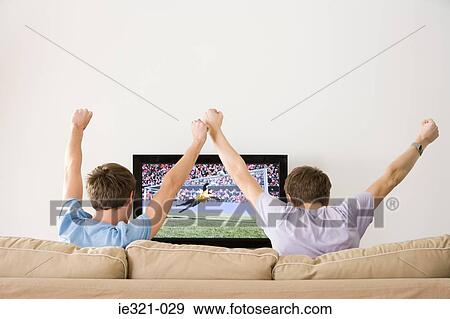 Stock Photo - Two young men cheering at football on the tv. Fotosearch