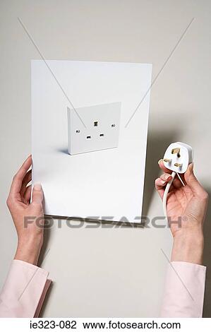 Stock Image - A woman holding a photograph of a socket and a plug. Fotosearch