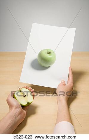 Stock Image - A woman holding a photograph of an apple. Fotosearch