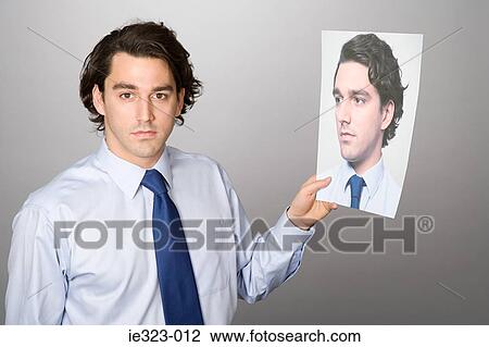 Stock Image - Portrait of a man holding a photograph of himself. Fotosearch