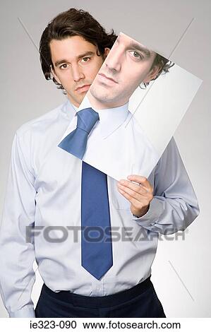 Stock Image - Portrait of a man holding a photograph of himself. Fotosearch