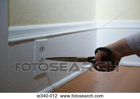 Stock Image - Child poking scissors in electrical socket. Fotosearch
