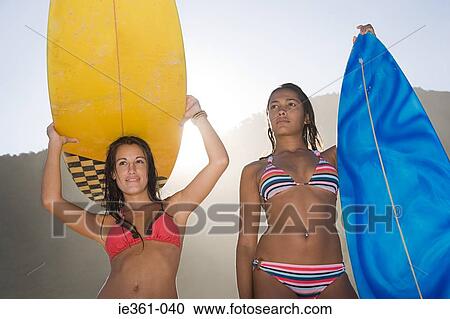 Stock Image - Portrait of teenage girls holding surfboards. Fotosearch