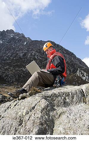 A man using a laptop on a rock View Large Photo Image Stock Image - A man using a laptop on a rock. Fotosearch