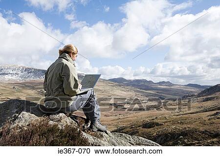 A woman sat on a rock using a laptop View Large Photo Image Stock Image - A woman sat on a rock using a laptop. Fotosearch