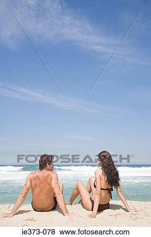 Stock Photo - Young couple sitting on a beach. Fotosearch