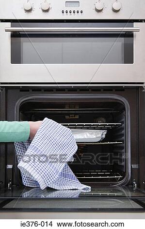 Picture - Person putting dish in oven. Fotosearch