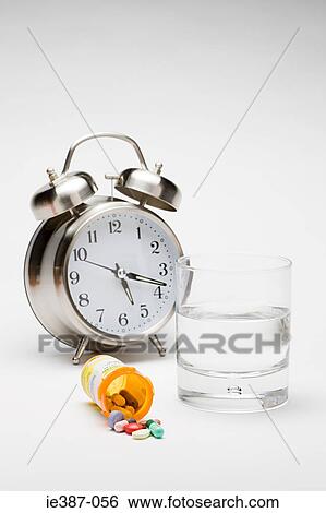 Stock Photograph - Alarm clock tablets and a glass of water. Fotosearch