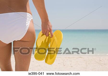 Stock Image - A young woman holding flip flops. Fotosearch