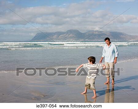 Picture - Father and son throwing stones in sea. Fotosearch