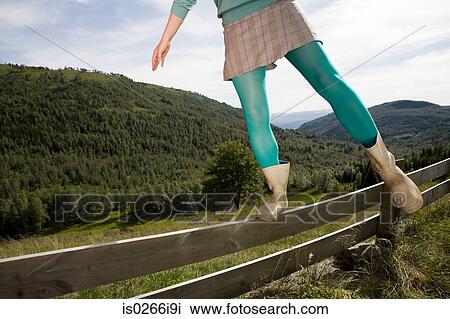 Stock Image - Woman balancing on a wooden fence. Fotosearch