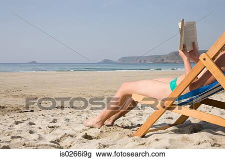 Stock Image - Woman reading a book on an empty beach. Fotosearch